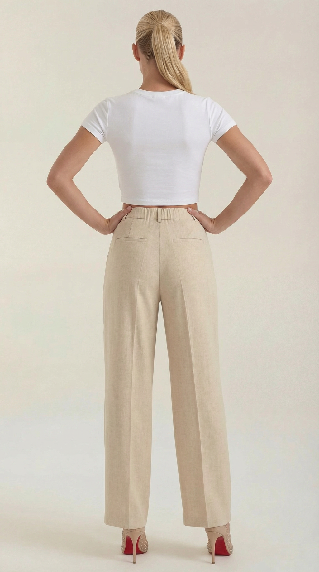 Beige high-rise pleated wide-leg pants on model, back view with waistband.